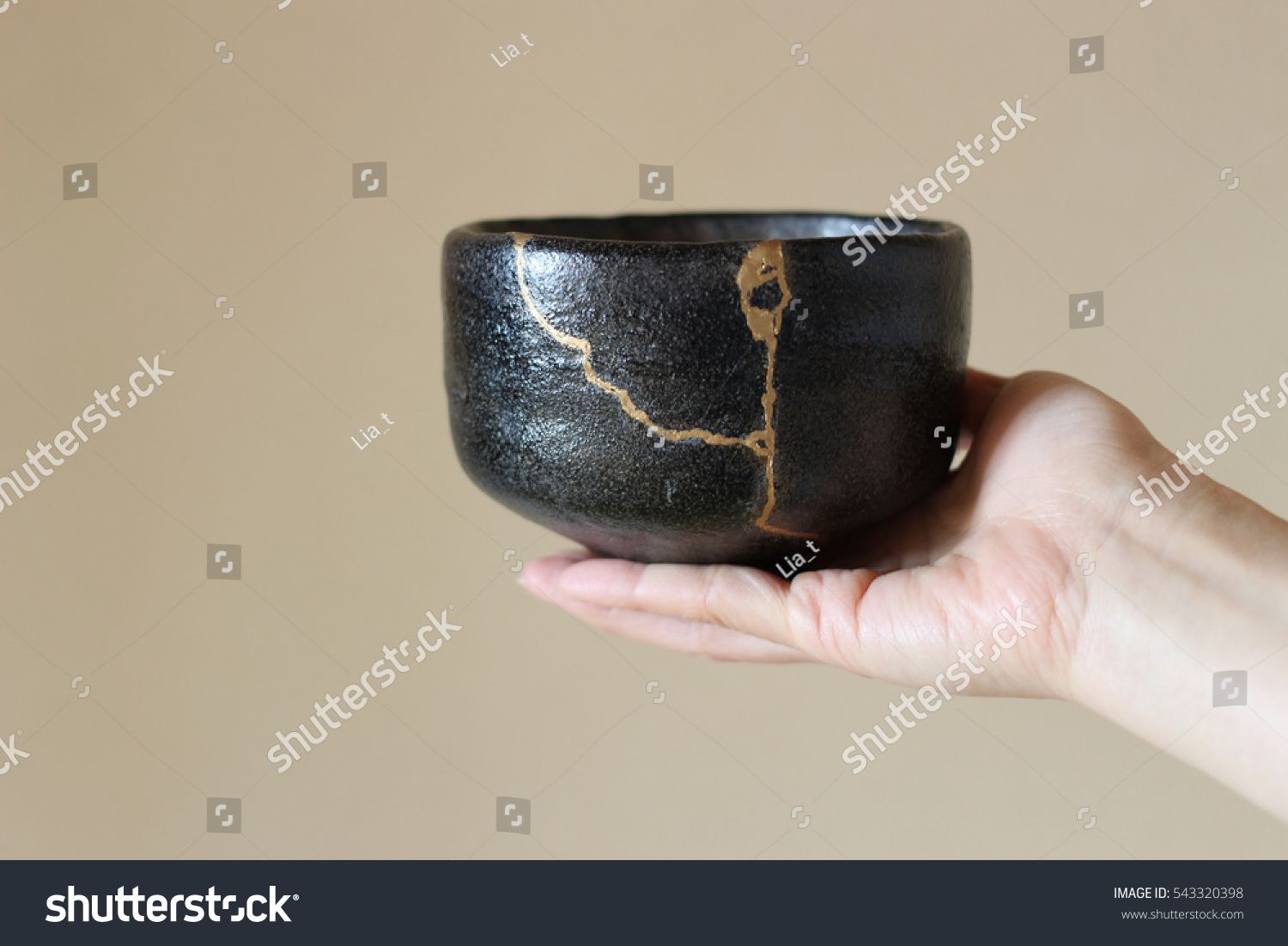 An image of a small, black Japanese bowl with a crack running through it. The crack has been mended or filled in with gold.